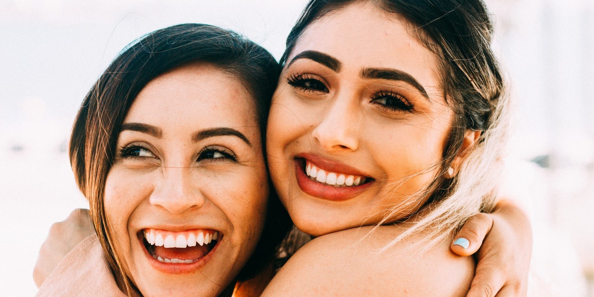 two girls hugging, one smiling one laughing two girls hugging, one smiling one laughing