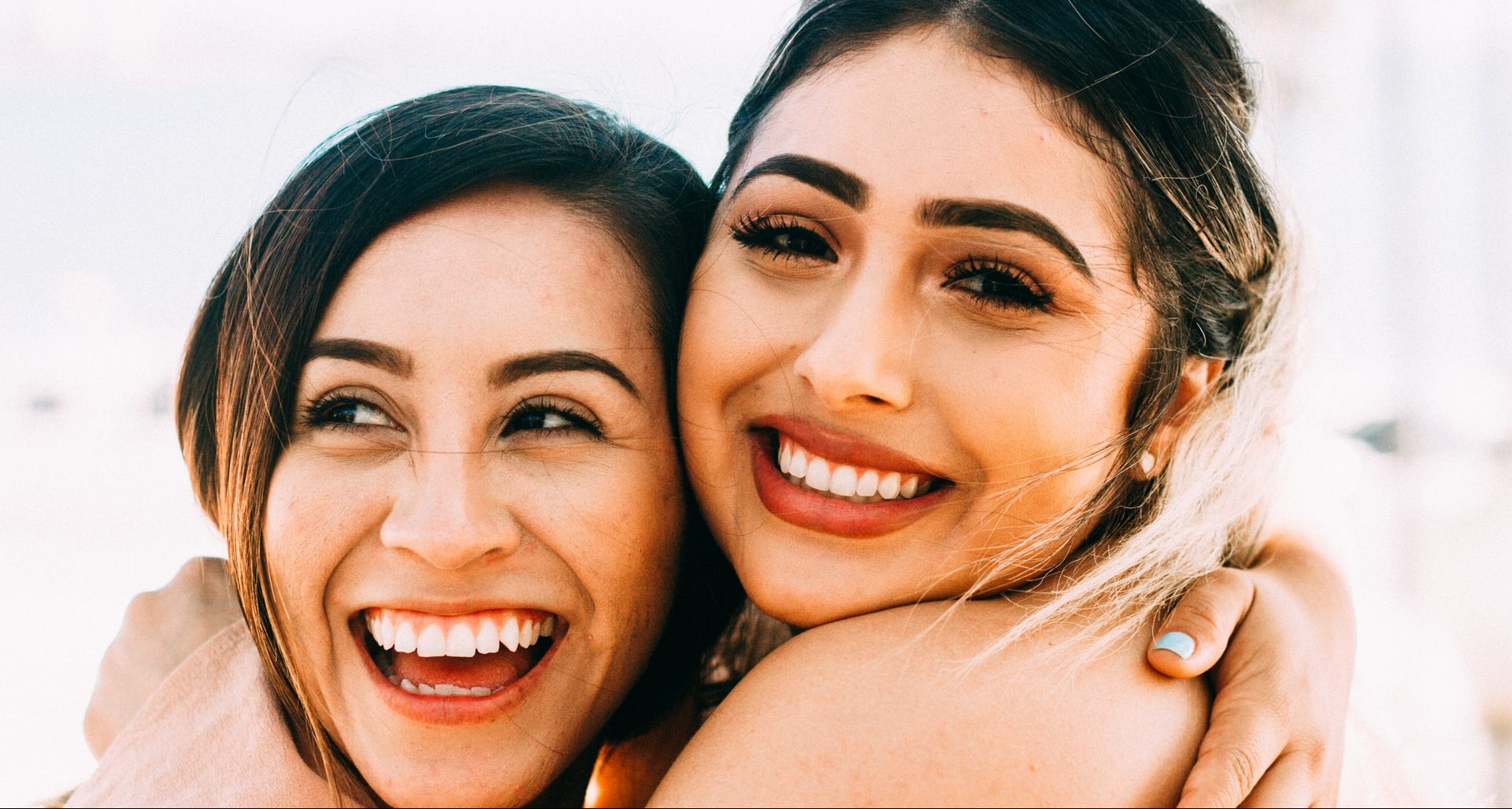 two girls hugging, one smiling one laughing two girls hugging, one smiling one laughing